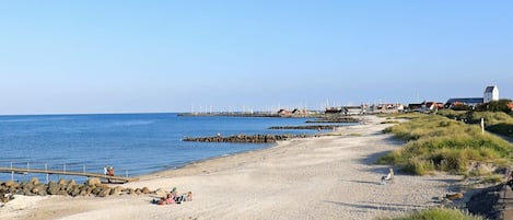 Une plage côtière bordée d’une côte rocheuse, une jetée sur laquelle sont installées des éoliennes, et un phare en arrière-plan.