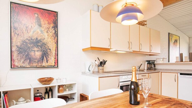 Una cocina moderna con armarios blancos, una mesa de comedor de madera y un cuadro grande en la pared.