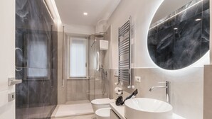A modern bathroom with a glass-enclosed shower, a large round mirror, and a white sink. - THE FIFTH PROPERTIES ROME (Roma)