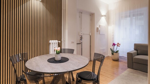 A modern living room with a round dining table, black chairs, a beige sofa, and a potted plant. - THE FIFTH PROPERTIES ROME (Roma)