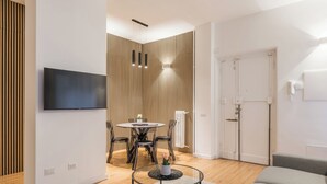 A modern living room with a flat-screen TV mounted on the wall, a round glass coffee table with a decorative item, a dining area with a round table and chairs, and a sliding door leading to another room. - THE FIFTH PROPERTIES ROME (Roma)