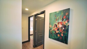 Un pasillo con suelo de madera, una puerta y un cuadro en la pared.