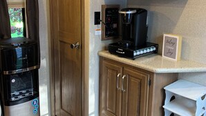 Eine kleine Küche mit Kaffeemaschine, Kaffeezubereiter und einem Schrank mit einem Bilderrahmen.