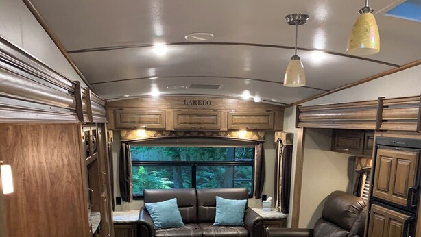 Ein kompaktes Wohnmobil-Interieur mit Küchenzeile, Essbereich, einer Sitzecke mit Sofa und einem Fenster mit Blick ins Freie.