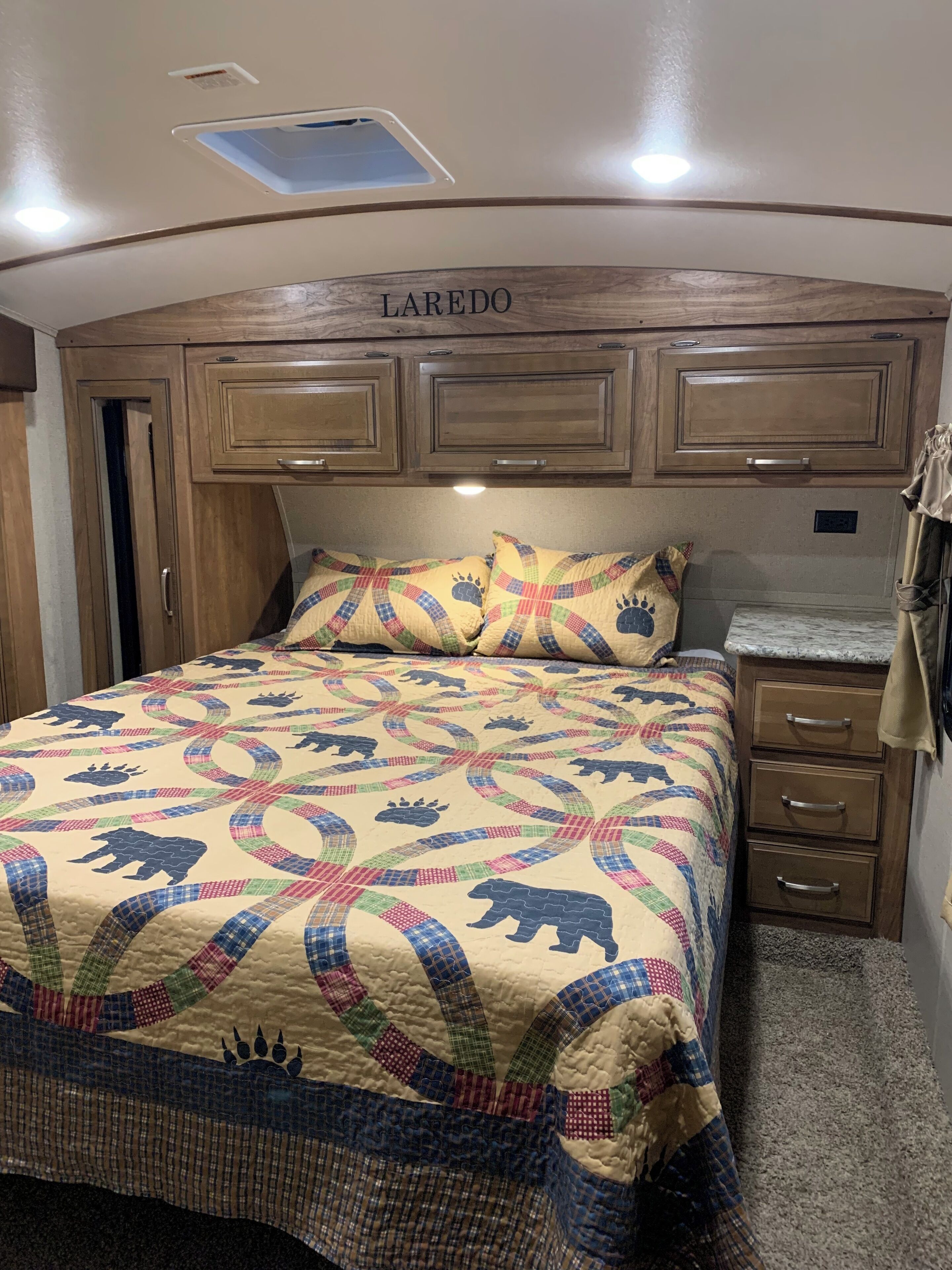 Un dormitorio con una cama, un cabecero identificado como 'LAREDO' y una mesita de noche con cajones.