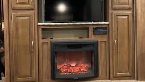 Ein Unterhaltungseinbau mit Holzvertäfelung, einem Flachbildfernseher und einem Kamin darunter.