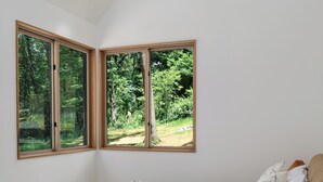 Un dormitorio con una cama, un ventilador de techo y tres ventanas con vistas a la vegetación.