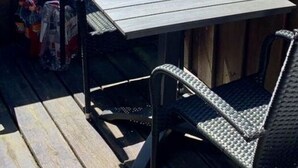 A small outdoor patio with a table and two chairs, surrounded by wooden fencing and a view of greenery. - Island Nest Modern Retreat (Fehmarn)