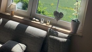 A room with a large window, a sofa, a lamp, and decorative items. - Island Nest Modern Retreat (Fehmarn)