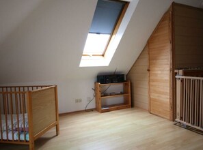 A room with a sloped ceiling, a wooden crib, a shelf unit, and a window. - Island Nest Modern Retreat (Fehmarn)