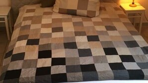 A bed with a quilted headboard, a checkered bedspread, and a bedside lamp. - Island Nest Modern Retreat (Fehmarn)