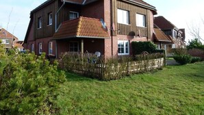 A two-story house with a sloped roof, a wooden fence, and a well-maintained lawn. - Island Nest Modern Retreat (Fehmarn)