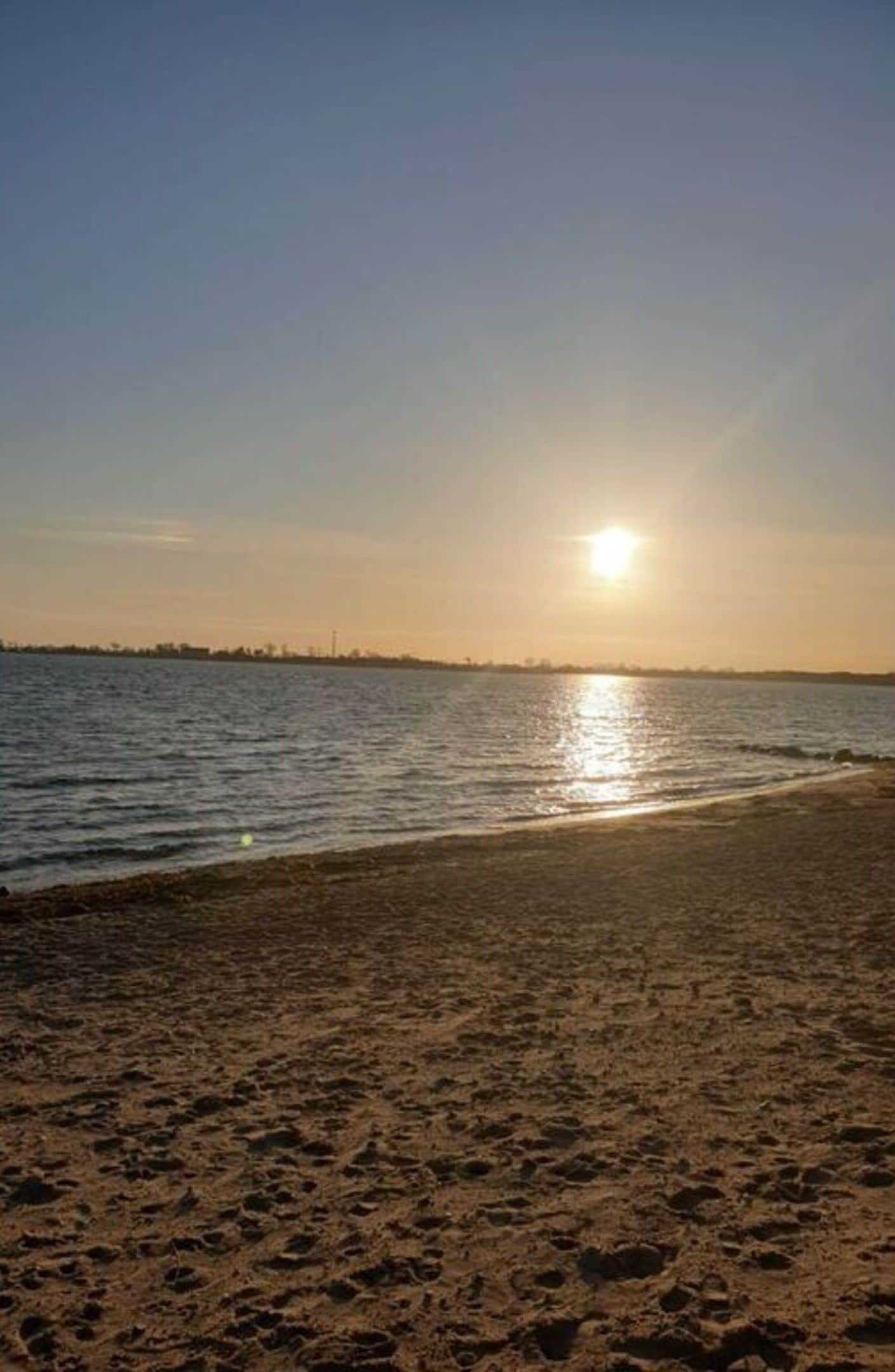 A beach with a clear sky and the sun setting over the water.