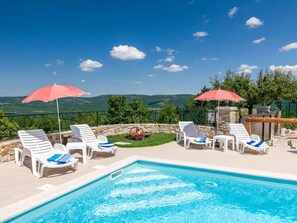 A poolside area with white lounge chairs and red umbrellas, overlooking a mountainous landscape. - Villa Montebello (Motovun)