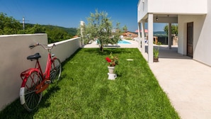 Una villa moderna con un césped cuidado, una bicicleta roja y una piscina al fondo.
