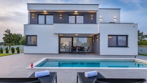 Una moderna casa a due piani con piscina, area salotto esterna e patio.