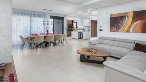 Un soggiorno moderno con divano, tavolino e zona pranzo con sedie e tavolo. Si intravede in secondo piano una cucina con isola centrale e tavolo da pranzo.