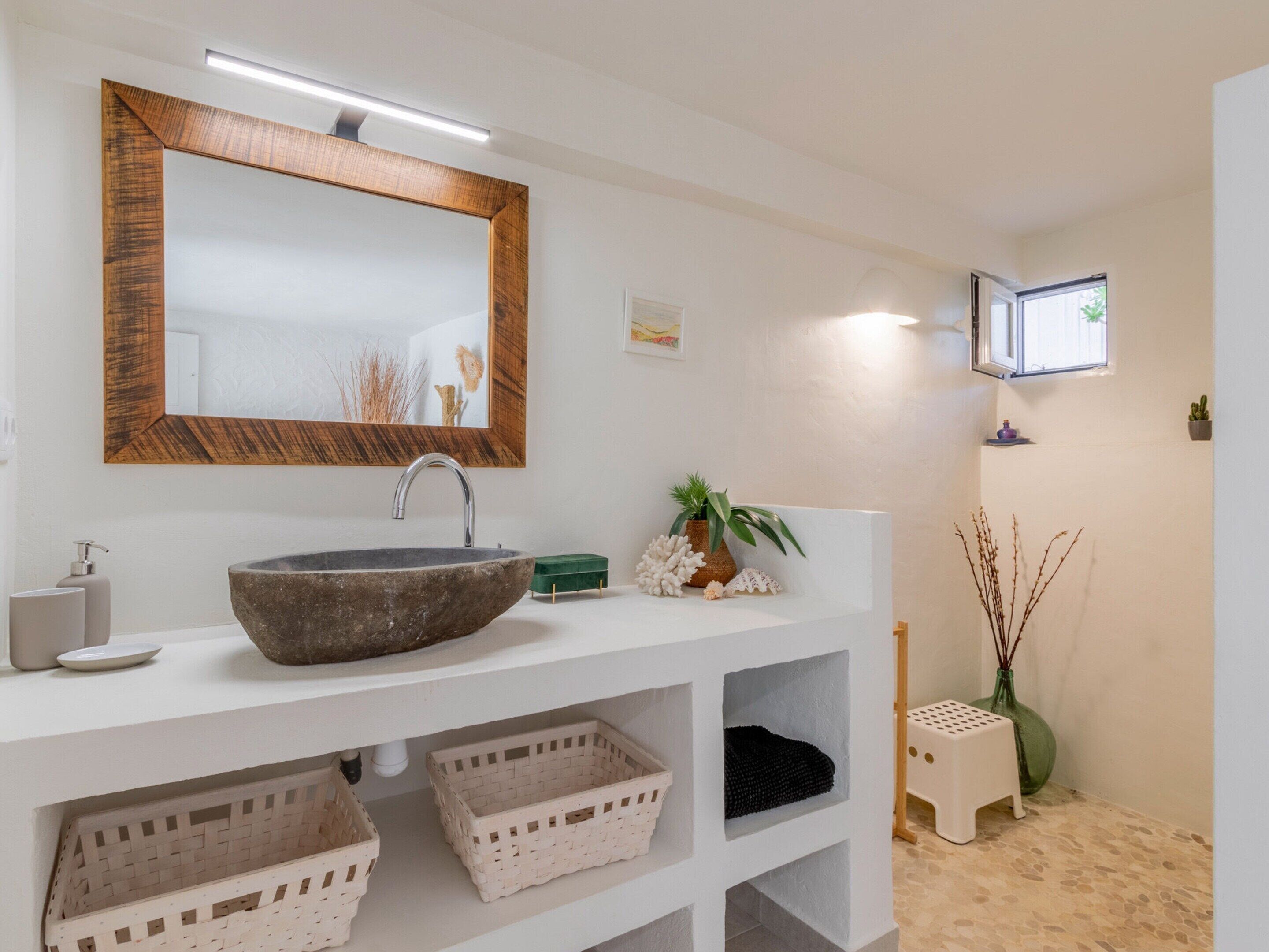 A bathroom with a large vessel sink, a wooden-framed mirror, and a small TV mounted on the wall.