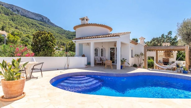 A poolside area with a white building, a pool, and a mountainous backdrop.