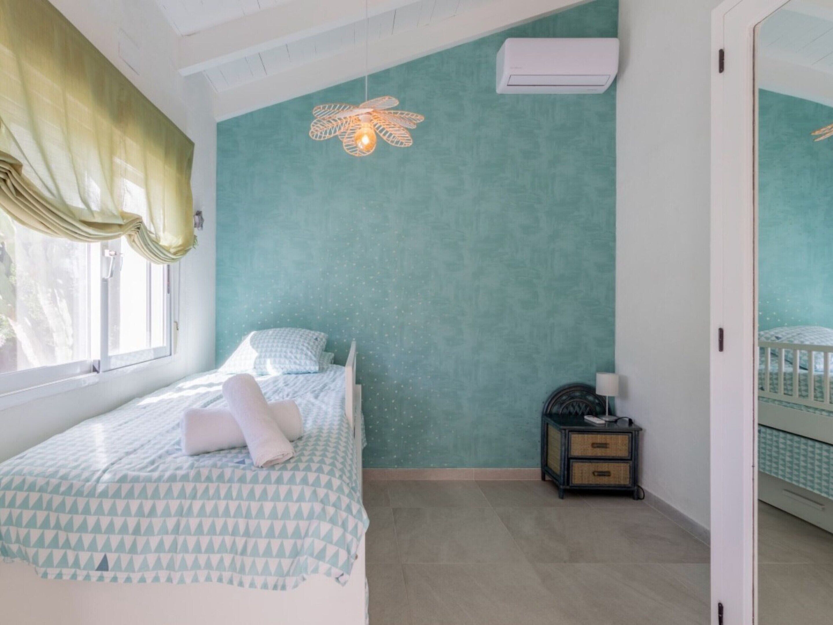 A bedroom with a bed, a nightstand, a wall-mounted air conditioner, and a window with curtains.