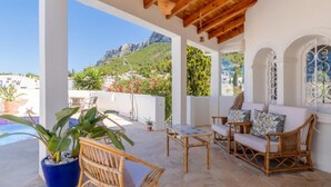 A covered outdoor seating area with wicker furniture, a pool, and a view of a mountainous landscape.