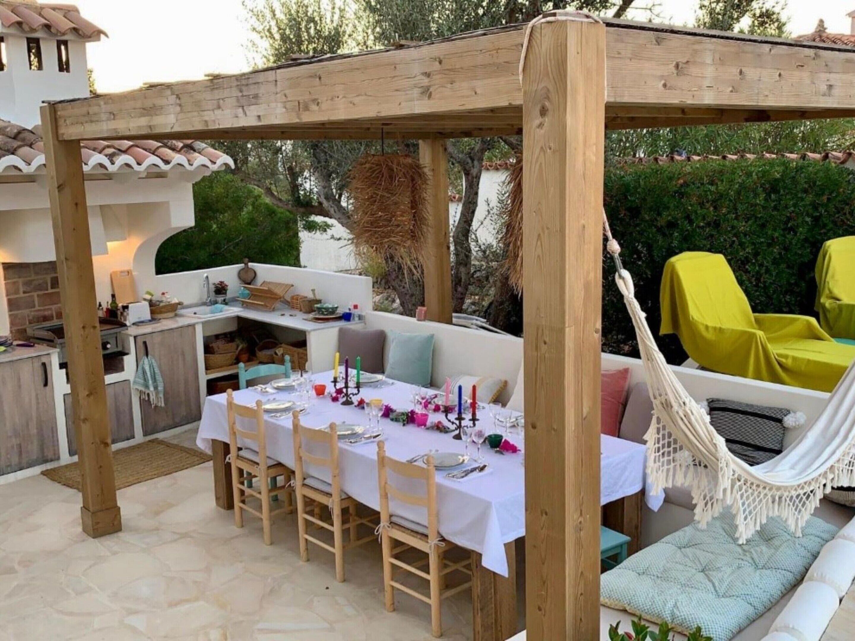 An outdoor patio with a wooden pergola, a dining table set for four, and a hammock.
