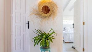 A hallway with a white door, a wall-mounted light fixture, and a potted plant on a stool.
