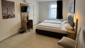 A modern hotel room with a bed, bedside tables, a desk with a chair, a TV, and a window with curtains. - Gap Hotel Event & more  (Langwedel)