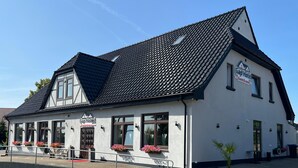 A white building with a black roof, labeled "Gap Hotel," featuring a balcony with flowers and a small garden area. - Gap Hotel Event & more  (Langwedel)