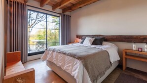 A bedroom with a large window, wooden headboard, and a bedside table with a lamp. - Casita Panadería Cozy House in San Simón (Valle de Bravo)