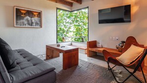 A modern living room with a sofa, a wooden coffee table, a chair, and a TV mounted on the wall. - Casita Panadería Cozy House in San Simón (Valle de Bravo)
