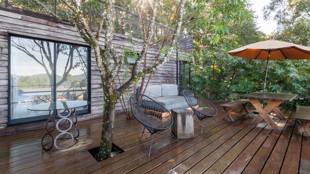 A wooden deck with a glass wall, outdoor seating, and a tree. - Casita Panadería Cozy House in San Simón (Valle de Bravo)