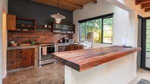 A modern kitchen with a large island, brick backsplash, and a view of greenery outside. - Casita Panadería Cozy House in San Simón (Valle de Bravo)