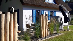 A house with a thatched roof, white walls, and blue shutters. There is a chair and a table outside. - Wave Rider Comfortable Holiday Residence (Glowe)