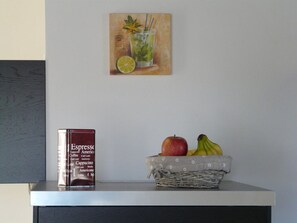 A coffee maker, a fruit basket, and a painting on a wall. - Swallow's Nest in the House by the Pond (Fehmarn)