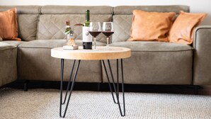 A round wooden table with a bottle of wine, two wine glasses, and a small plant on a beige carpeted floor. - Holiday Home in Zevenhuizen With Sauna (Zevenhuizen)