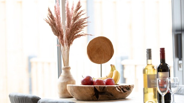 A dining table with a wooden bowl containing fruits, a vase with dried plants, and bottles of wine. - Holiday Home in Zevenhuizen With Sauna (Zevenhuizen)
