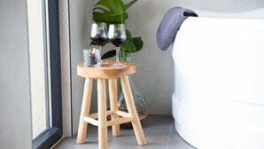 A wooden stool with two wine glasses and a candle, placed near a window with a plant in the background. - Holiday Home in Zevenhuizen With Sauna (Zevenhuizen)