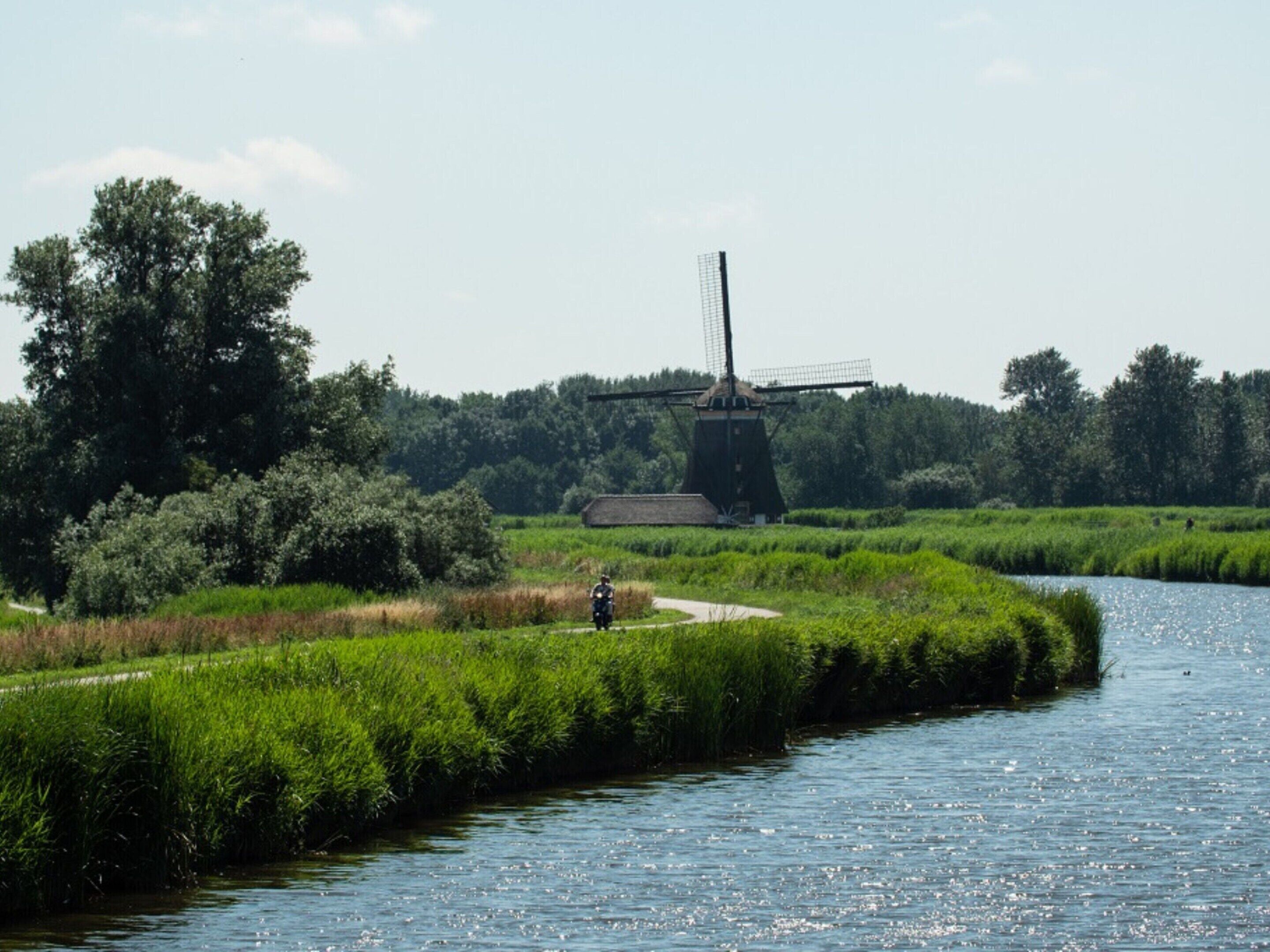 A river with a windmill in the background and a path along the riverbank.