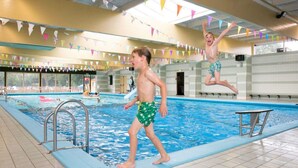 An indoor swimming pool with tiled floors and walls, a diving board, and colorful triangular flags. - Holiday Home in Zevenhuizen With Sauna (Zevenhuizen)
