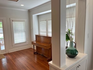 A spacious room with hardwood flooring, a wooden piano, and white walls. - 7 bedroom luxury, hot tub, porch, near downtown (San Antonio)