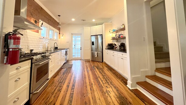 Une cuisine moderne avec des meubles blancs, des appareils électroménagers en acier inoxydable et un plancher en bois.
