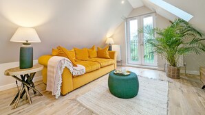 Una sala de estar moderna con un sofá amarillo, dos lámparas, un reposapiés verde y un ventanal con vistas a la vegetación.