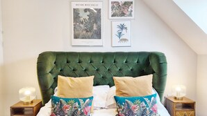 Un dormitorio con un cabecero verde capitonado, dos almohadas con diseño de cebra y dos obras de arte enmarcadas en la pared.