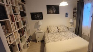 Een slaapkamer met een bed, nachtkastjes, een boekenkast en wanddecoratie.