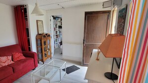 Een woonkamer met een rode bank, een glazen salontafel, een houten kast, een boekenkast en een deur naar een andere kamer.
