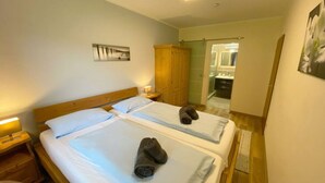 Hotellihuone, jossa on kaksi sänkyä, puinen pääty, yöpöytä lampulla, puinen vaatekaappi ja kylpyhuone, joka näkyy avoimesta ovesta.