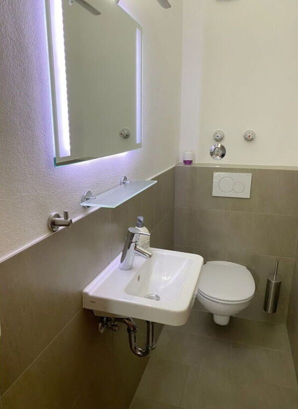 A bathroom with a white sink, a mirror, a toilet, and a soap dispenser. - Holiday Apartment No. 5 Bergschlossl (Oberaudorf)