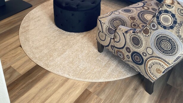 A modern living room with a blue sofa, patterned ottoman, and a round rug.