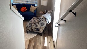 A staircase leading to a living area with a blue sofa, patterned ottoman, and a lamp.
